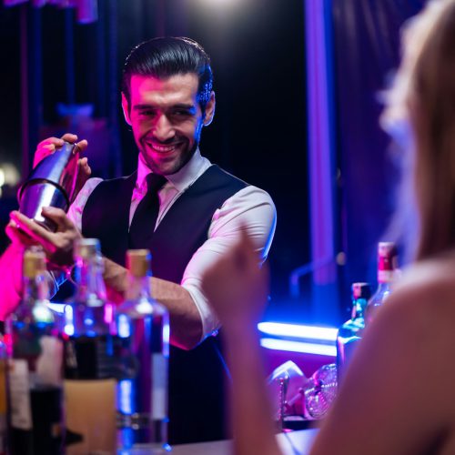 Caucasian profession bartender making a cocktail for women at a bar.