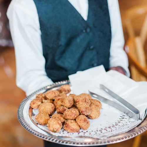 Vertical shot of a server wearing a dark teal vest serving snacks on a silver platter